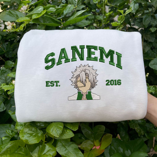 White Sanemi embroidered sweatshirt displayed outdoors on green foliage.