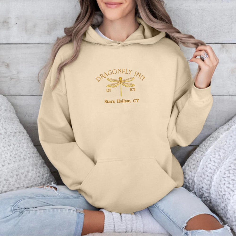 Sand Dragonfly Inn hoodie with golden dragonfly, cozy seated styling