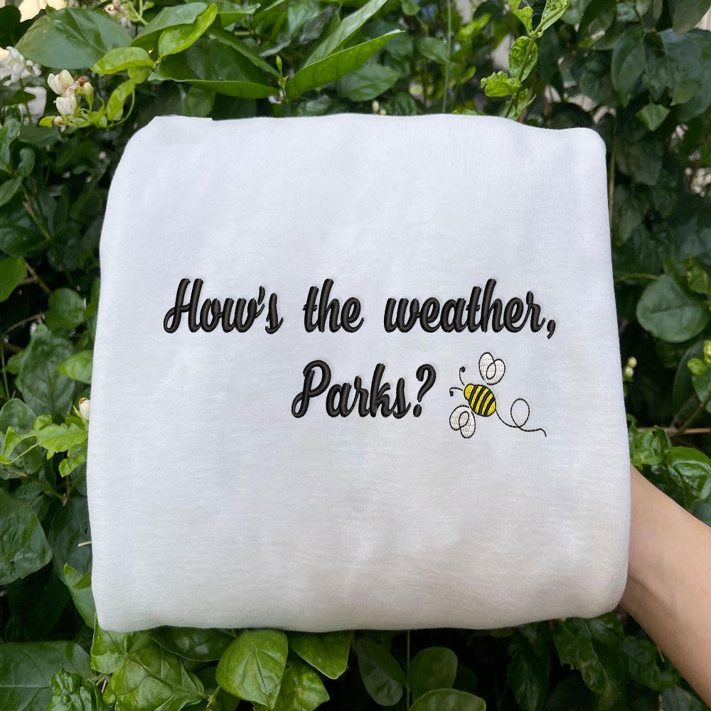 White Parks bee sweatshirt held outdoors, green leaves background