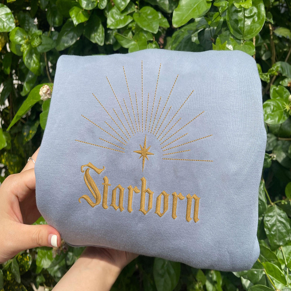Light blue Starborn radiant star sweatshirt held against leaves