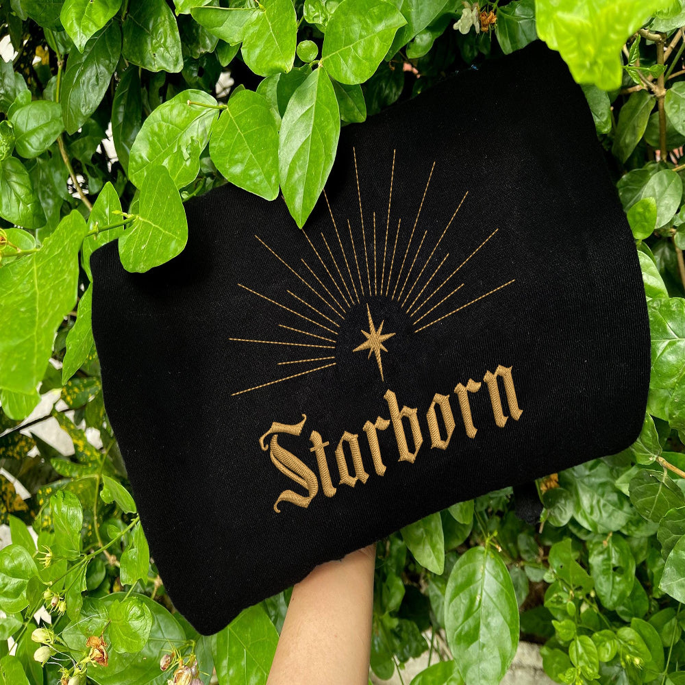 Black Starborn minimal gold design on dark foliage background