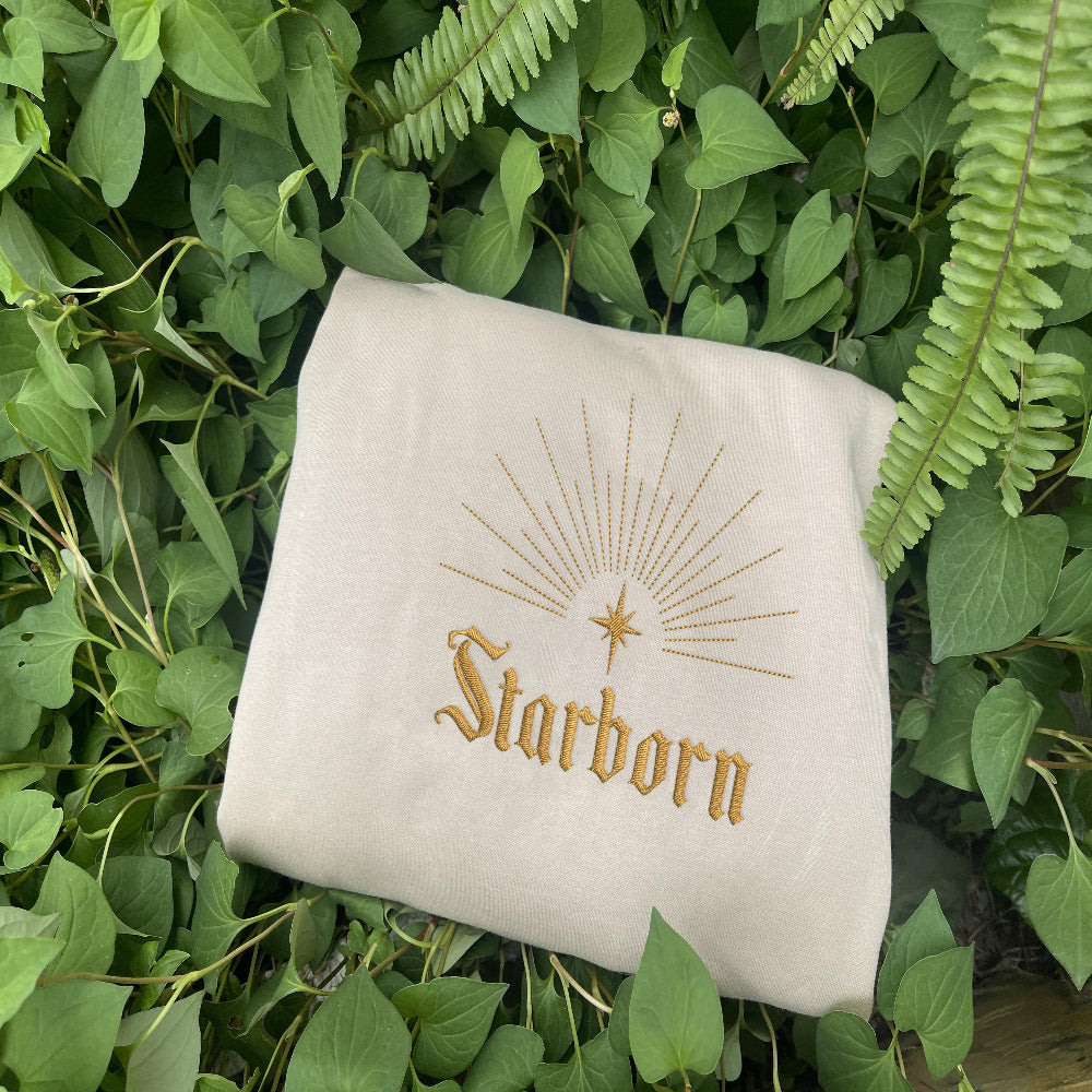Sand Starborn golden sunburst sweatshirt nestled in lush greenery