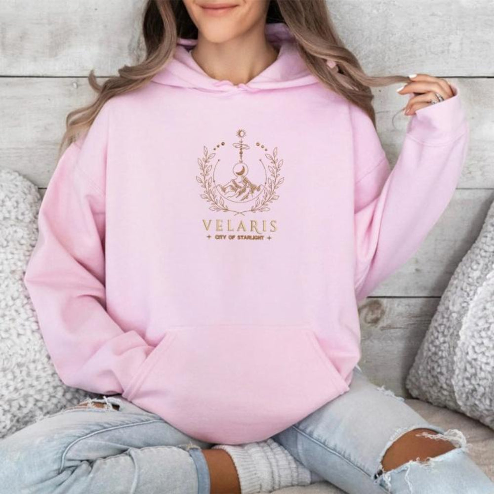 Pink Velaris hoodie, cozy seated pose on wooden floor