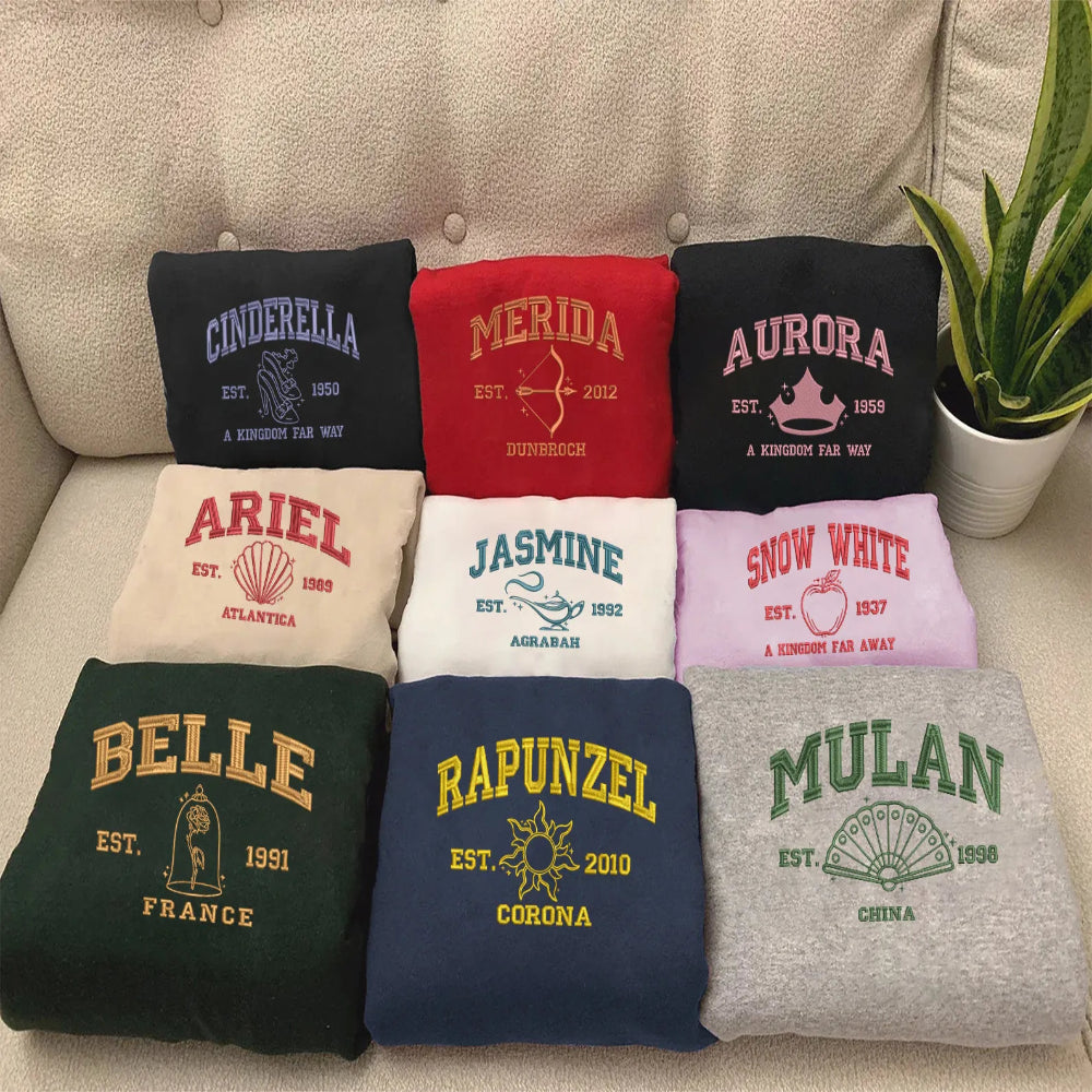 Assorted Folded Princess Sweatshirts On Couch Including Belle, Rapunzel, Merida,...