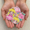 Hands Holding Collection Of Kawaii Peach Patches Including Crown, Umbrella
