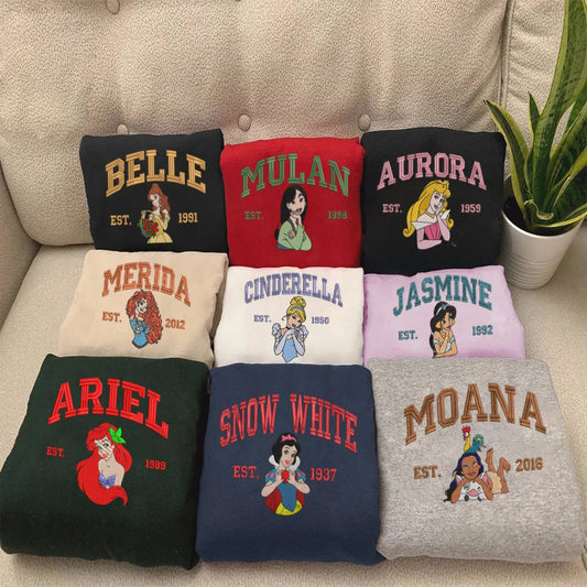 Folded Disney Princess Sweatshirts Displayed On Couch: Belle, Mulan, Aurora