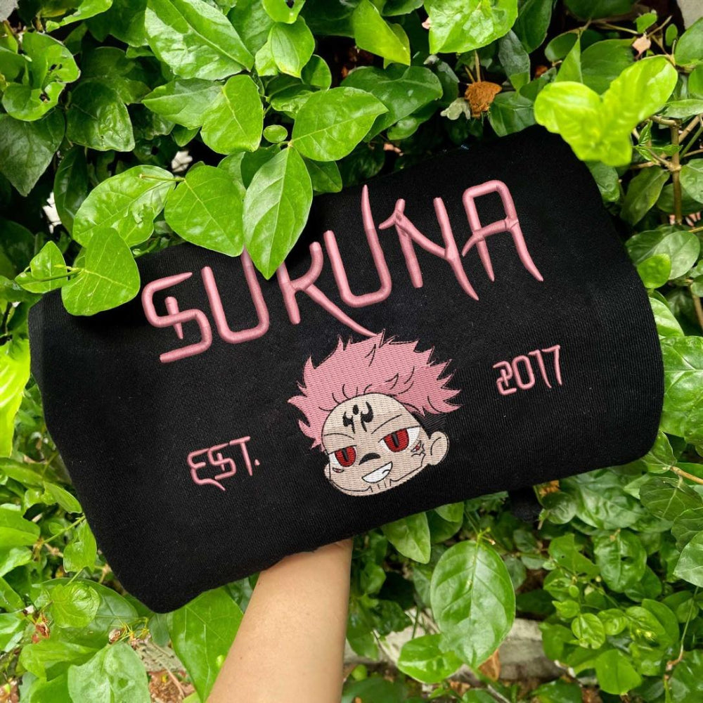Black Sukuna Est.2017 pink embroidery sweatshirt, green foliage background