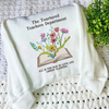 Folded Sweater Displaying Embroidered Wildflowers Emerging From Open Book