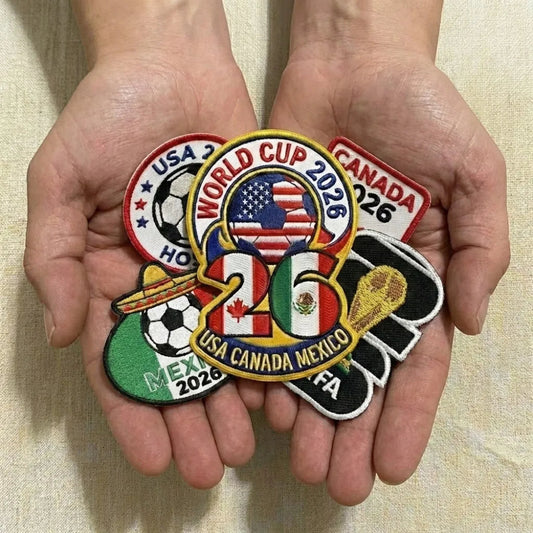 Hands Holding Assorted FIFA World Cup USA Canada Mexico Patches